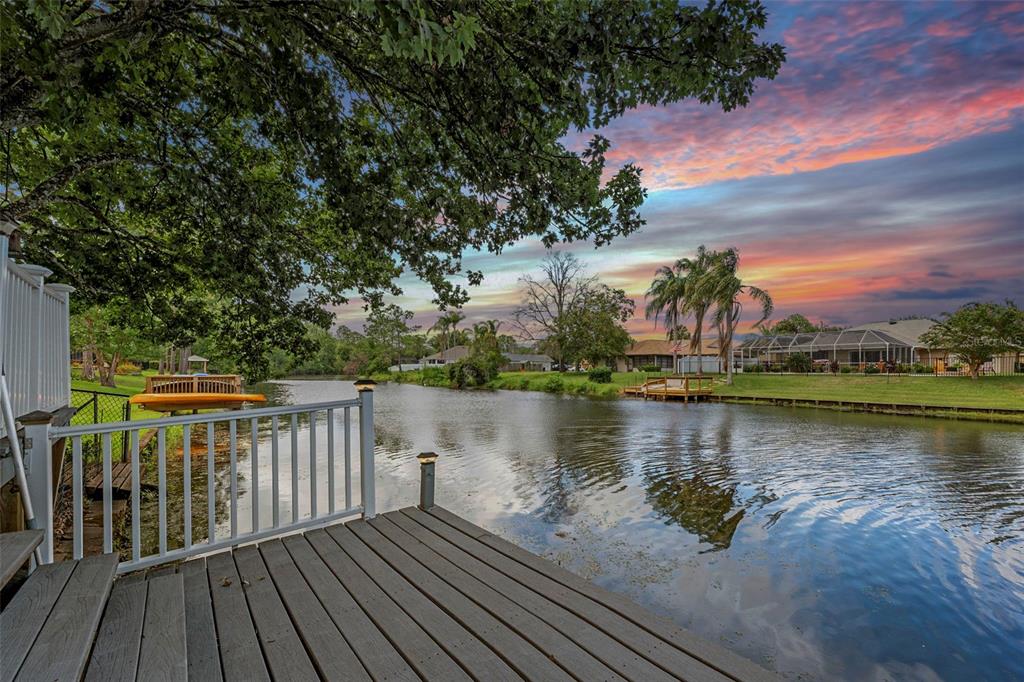 A wooden deck overlooks a calm canal with houses and trees under a sunset sky — 52 BUTTONWORTH DRIVE, PALM COAST, FL