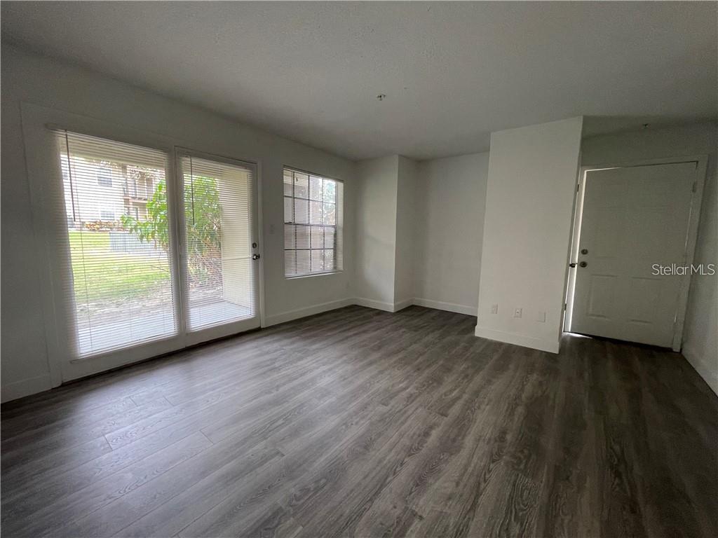 An empty room features wood-look flooring, white walls, a sliding glass door, and a window — 232 AFTON SQUARE UNIT 112, ALTAMONTE SPRINGS, FL