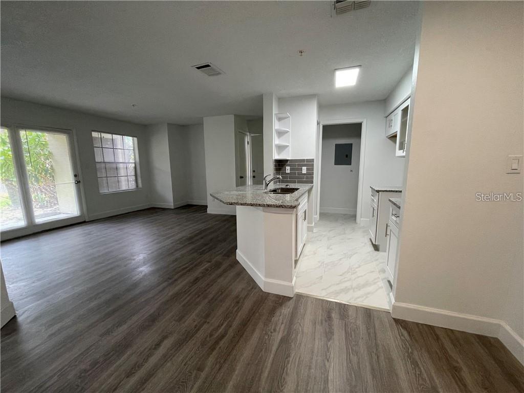 A kitchen with granite countertops and white cabinets opens into a living area with flooring — 232 AFTON SQUARE UNIT 112, ALTAMONTE SPRINGS, FL