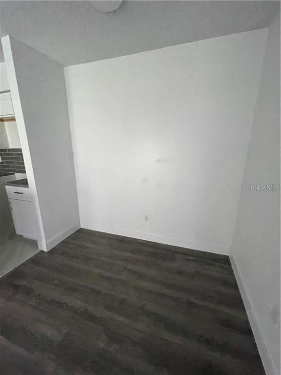 An empty room with white walls and dark wood-look flooring next to a kitchen area — 232 AFTON SQUARE UNIT 112, ALTAMONTE SPRINGS, FL