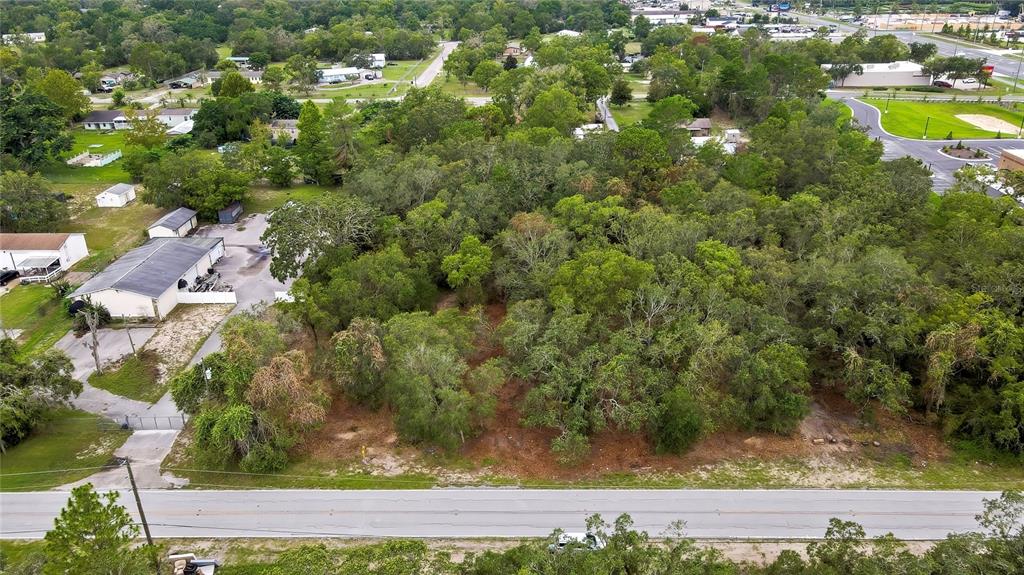 An aerial view shows a wooded, undeveloped lot situated between a road and commercial buildings — 0 OLD SHADY HILLS ROAD, SPRING HILL, FL