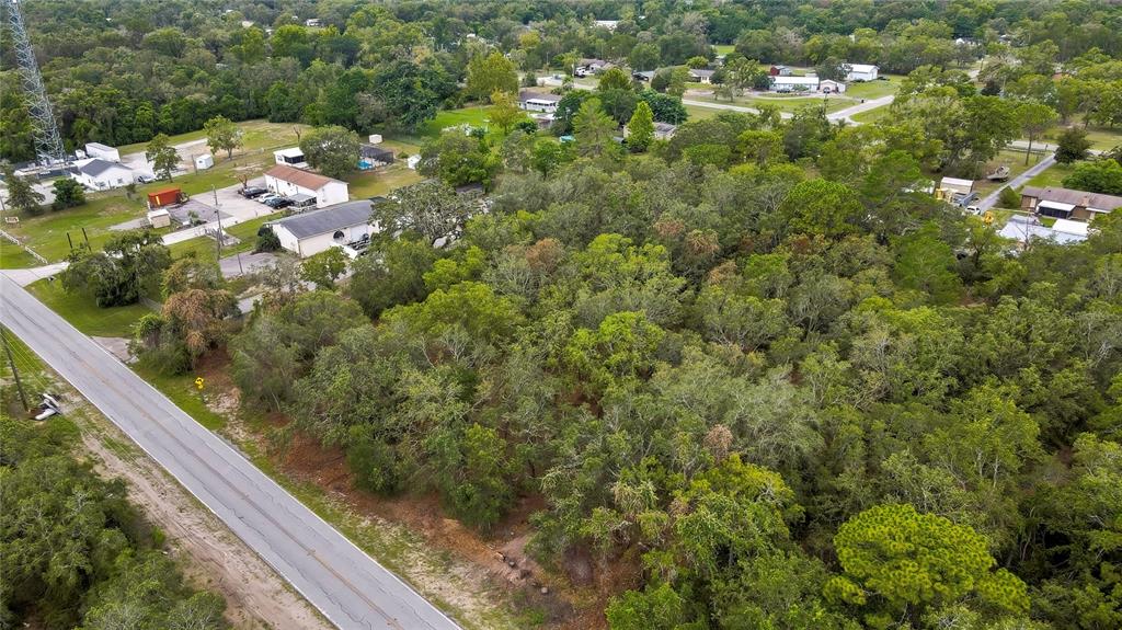 An aerial view shows a wooded lot adjacent to a paved road and nearby buildings — 0 OLD SHADY HILLS ROAD, SPRING HILL, FL