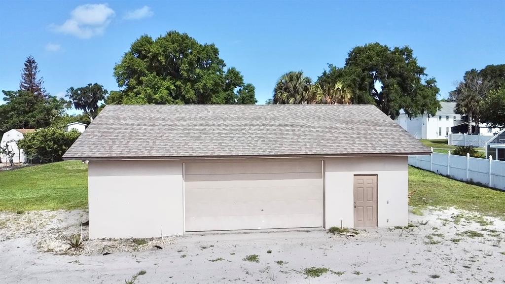 A detached garage with a beige exterior, a large roll-up door, and a single entry door — 3155 LAKESHORE DRIVE, MOUNT DORA, FL
