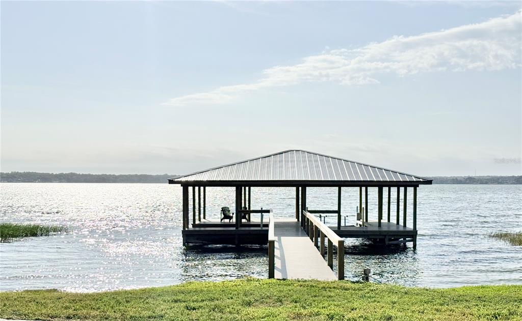 A covered boat dock with a walkway extends into a large lake — 3155 LAKESHORE DRIVE, MOUNT DORA, FL