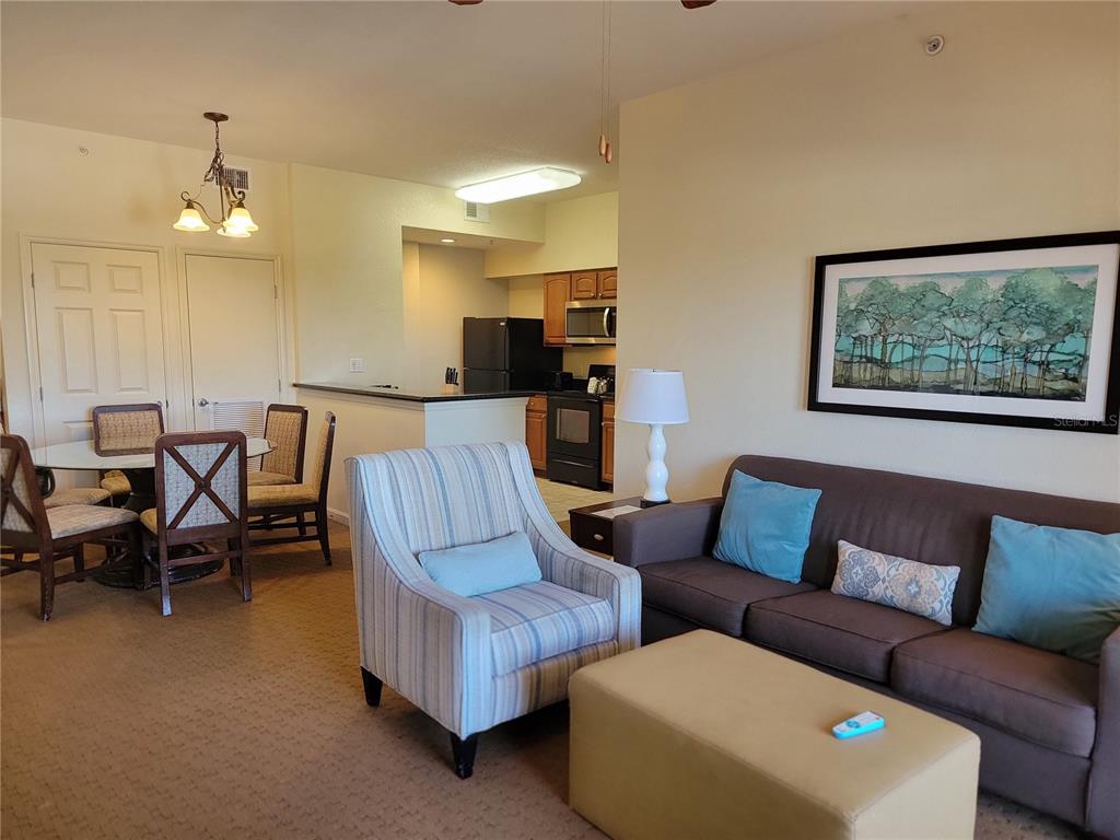 A living room with a striped armchair, a television, and a view of a balcony — 8101 RESORT VILLAGE DRIVE UNIT 31212, ORLANDO, FL