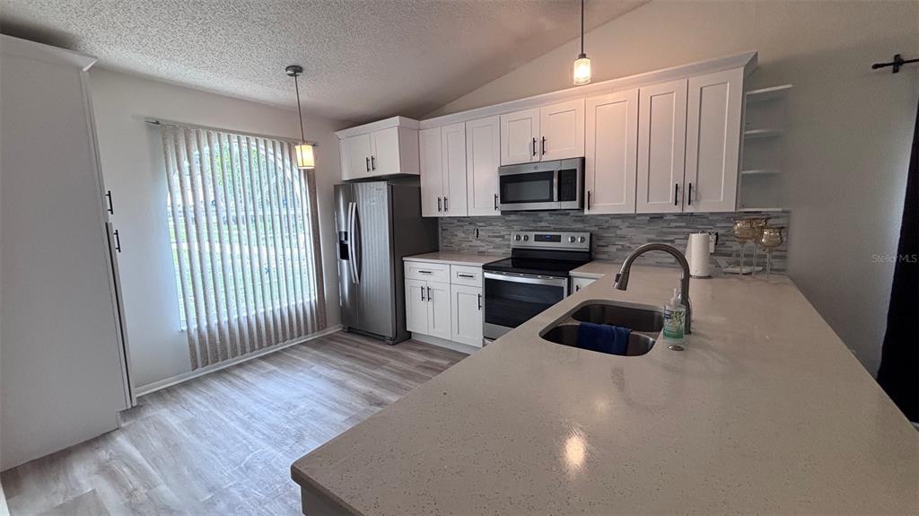 A kitchen features white cabinets, stainless steel appliances, a quartz island, and light wood flooring — 6518 SPRING LAND COURT, ORLANDO, FL