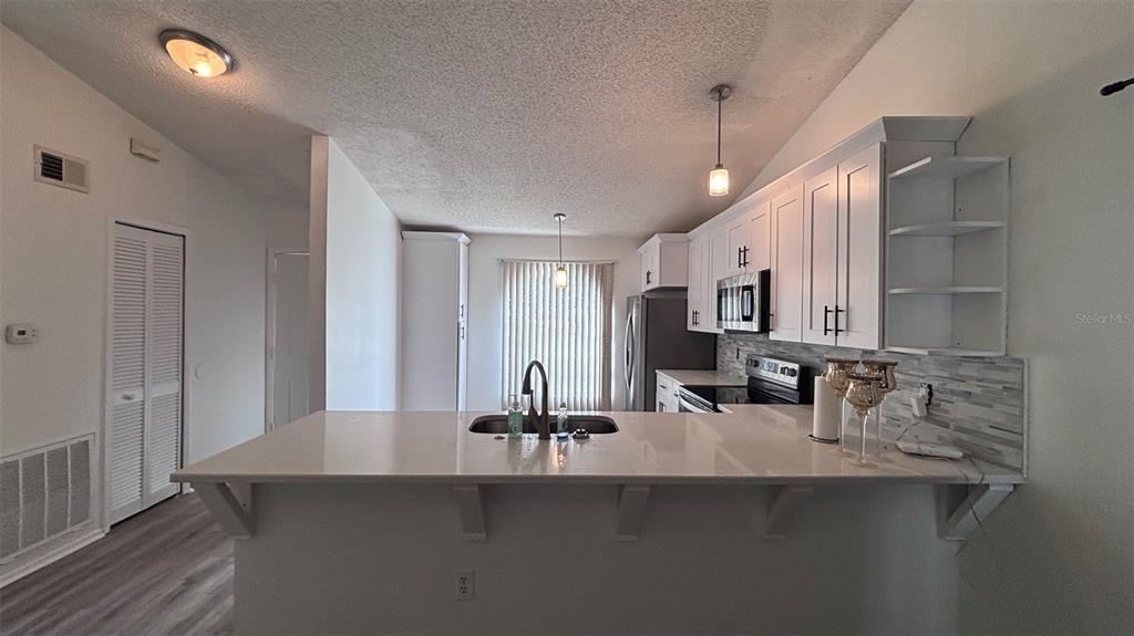 A kitchen features white cabinets, a quartz island countertop, and a tiled backsplash — 6518 SPRING LAND COURT, ORLANDO, FL
