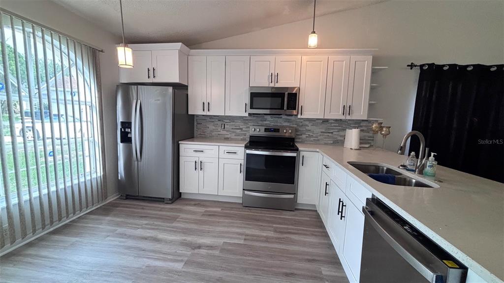 A kitchen features white cabinets, stainless steel appliances, a tiled backsplash, and light wood flooring — 6518 SPRING LAND COURT, ORLANDO, FL