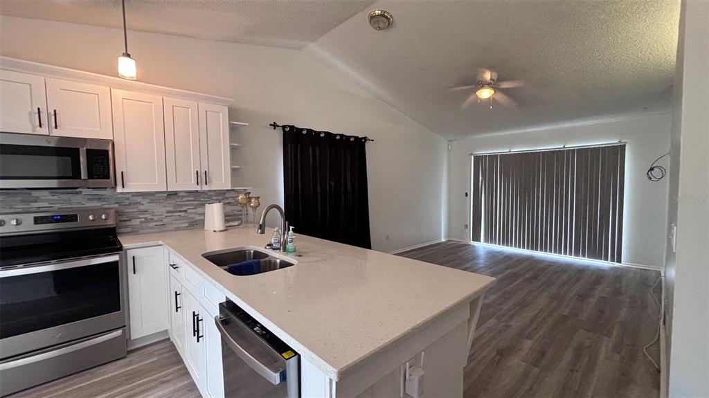 A kitchen with white cabinets and quartz countertops opens into a living area with flooring — 6518 SPRING LAND COURT, ORLANDO, FL