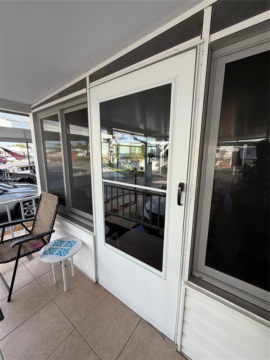 A white screen door leads to a tiled porch with a chair and small table — 6444 SE 51st Lane, Okeechobee FL 34974, OKEECHOBEE, FL