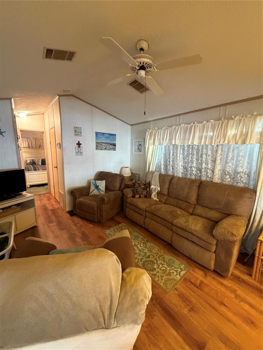 A living room features a brown sofa, a matching armchair, wood-look flooring, and a ceiling fan — 6444 SE 51st Lane, Okeechobee FL 34974, OKEECHOBEE, FL