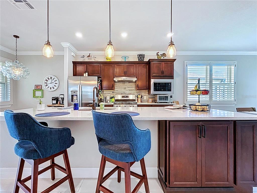 A kitchen features dark wood cabinets, a white island with blue stools, and pendant lighting — 19537 SHIP WHEEL WAY, LAND O LAKES, FL