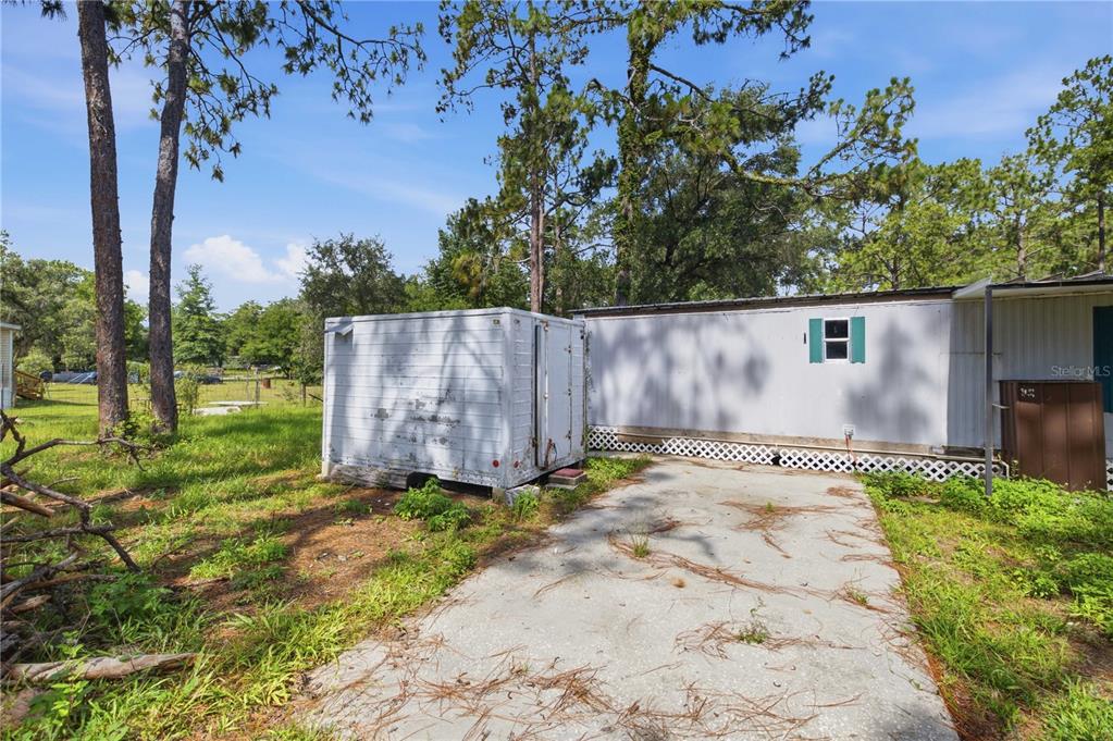 A white storage trailer sits on a concrete pad next to a mobile home exterior — 2290 SE 141ST AVENUE, MORRISTON, FL