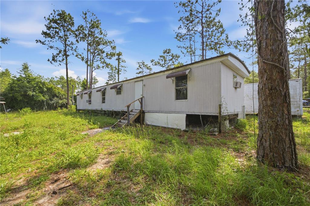 A single-story mobile home sits on a grassy lot surrounded by tall pine trees — 2290 SE 141ST AVENUE, MORRISTON, FL