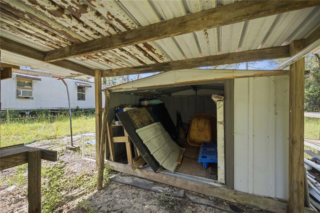 A small, weathered metal storage shed sits beneath a rustic, open-sided wooden carport structure — 2290 SE 141ST AVENUE, MORRISTON, FL