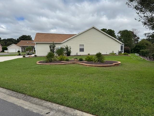 A side view of a beige, single-story house with a lawn and a landscaped garden bed — 903 RAMOS DRIVE, THE VILLAGES, FL