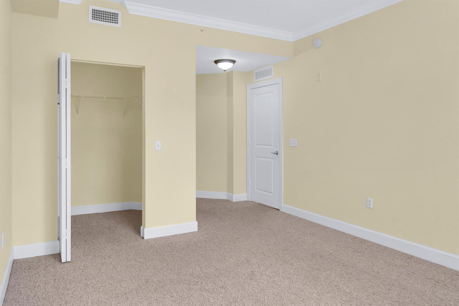 A carpeted bedroom features a walk-in closet, a white door, and light yellow walls — 1690 Renaissance Commons Boulevard # 1103, Boynton Beach FL 33426, BOYNTON BEACH, FL