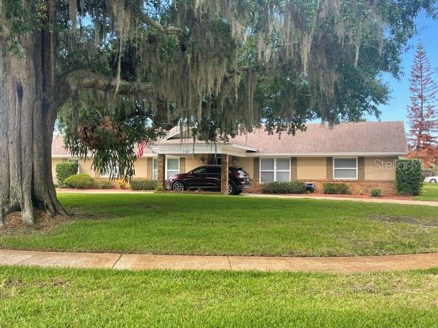 A single-story house with a tan exterior and a dark roof sits behind a large tree — 130 SPRINGWOOD TRAIL, ALTAMONTE SPRINGS, FL