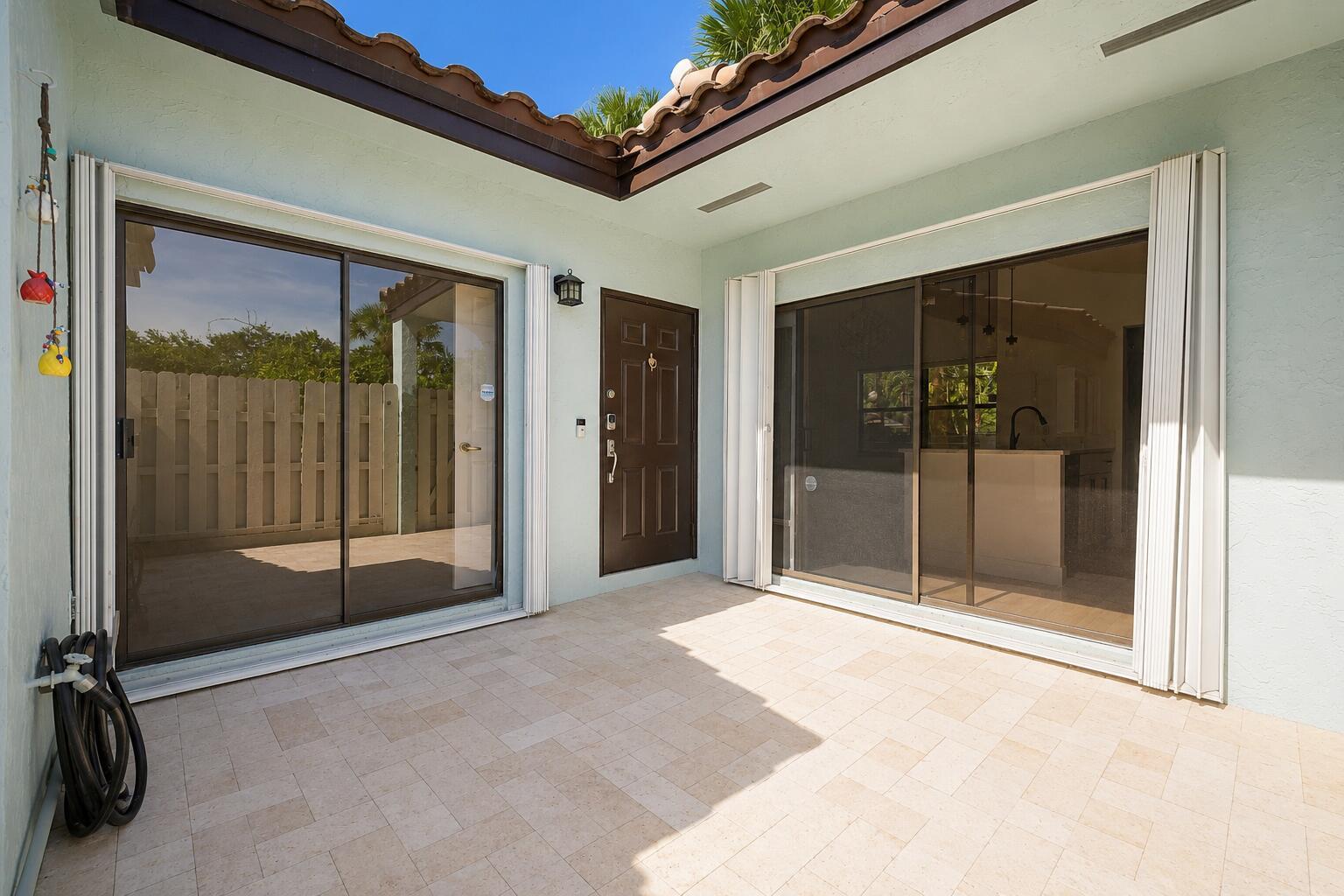 A paved outdoor patio features two sliding glass doors and a brown entry door — 22354 Pineapple Walk Drive, Boca Raton FL 33433, BOCA RATON, FL