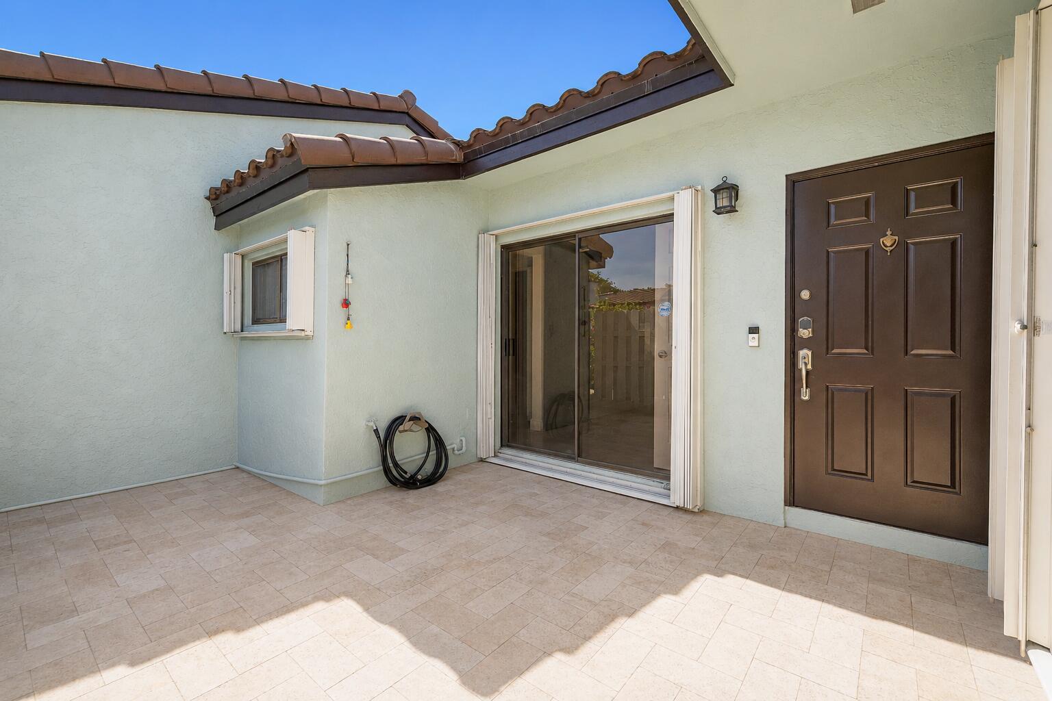 A paved patio area features a brown front door, a sliding glass door, and stucco walls — 22354 Pineapple Walk Drive, Boca Raton FL 33433, BOCA RATON, FL