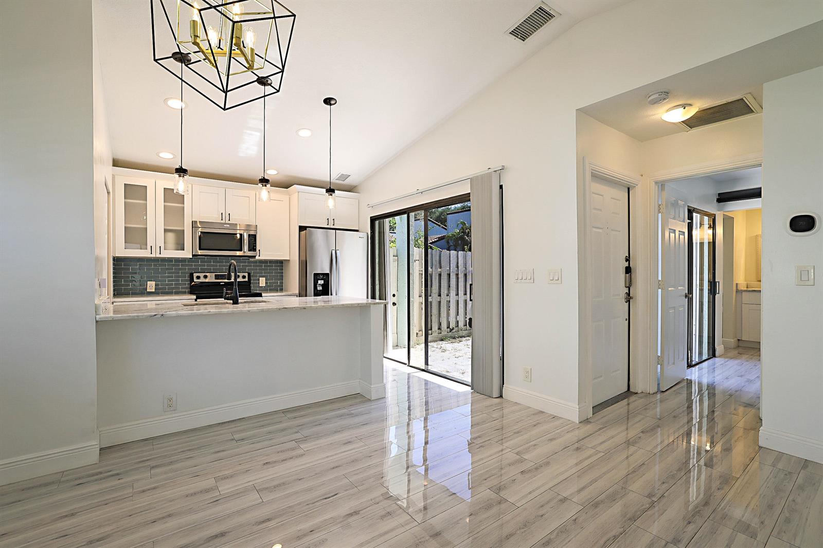 A kitchen with white cabinets, a marble-topped island, and gray tile flooring opens to a patio — 22354 Pineapple Walk Drive, Boca Raton FL 33433, BOCA RATON, FL