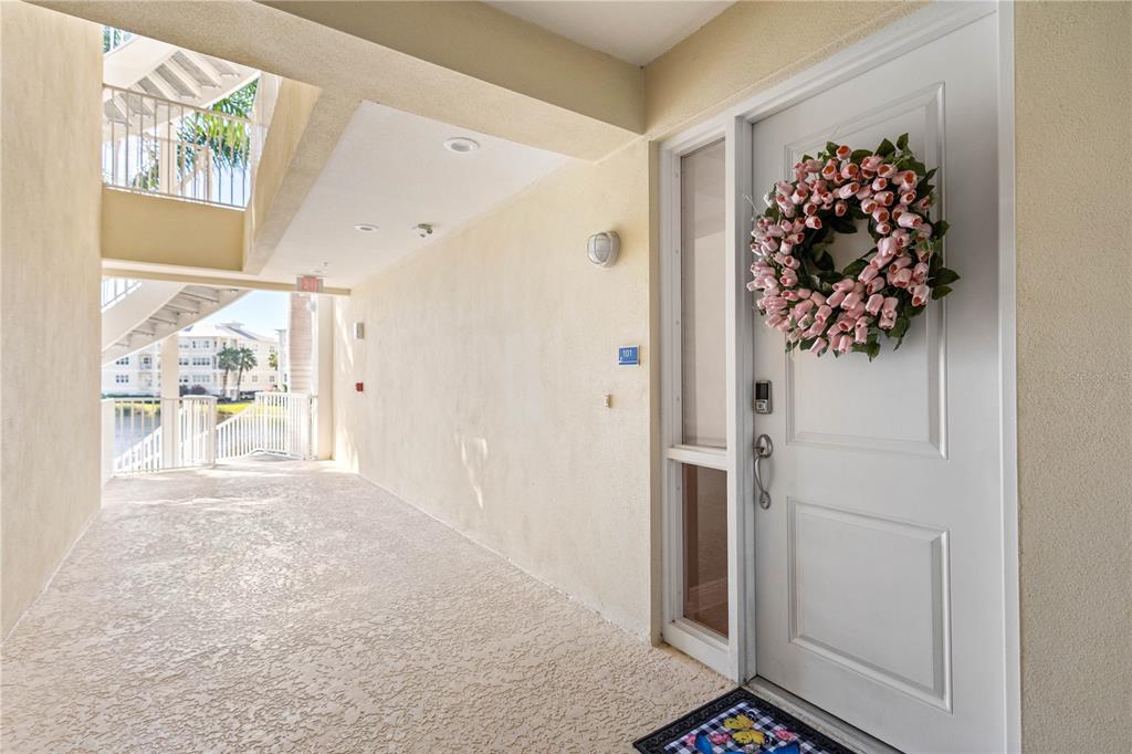 A white front door with a floral wreath opens onto a covered outdoor walkway — 3431 79TH STREET CIRCLE W UNIT 101, BRADENTON, FL