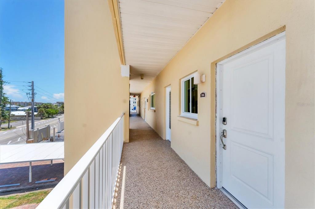 An exterior apartment walkway features a white railing, beige walls, and a white door — 1200 TARPON CENTER DRIVE UNIT 306, VENICE, FL