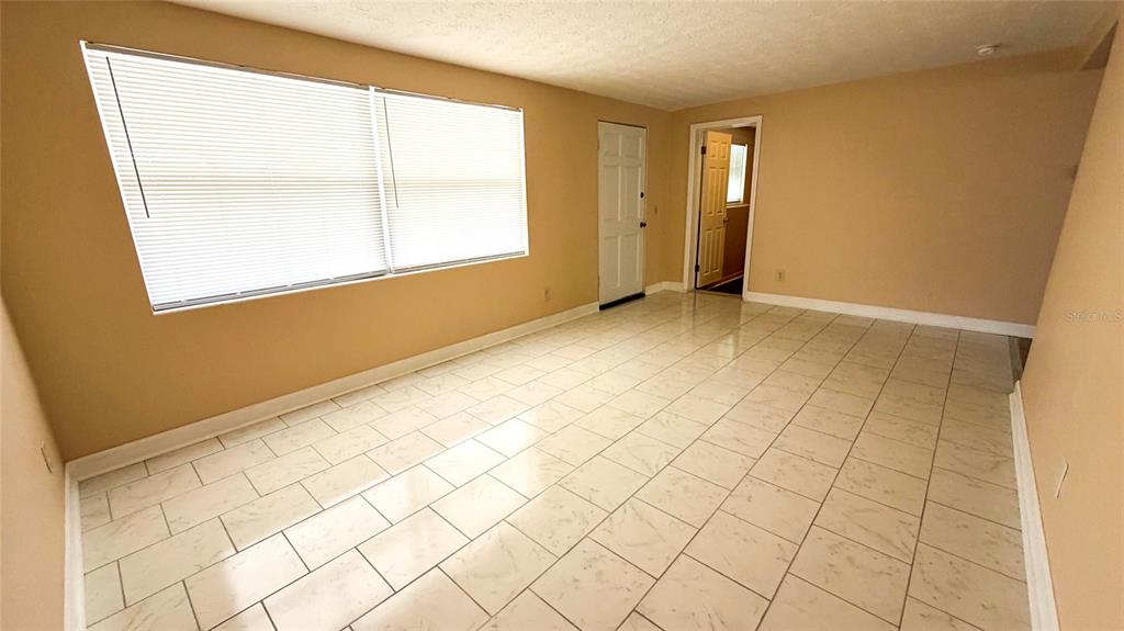 An empty room with light-colored tile flooring, beige walls, and a large window with blinds — 4102 HIGHLAND LOOP, NEW PORT RICHEY, FL