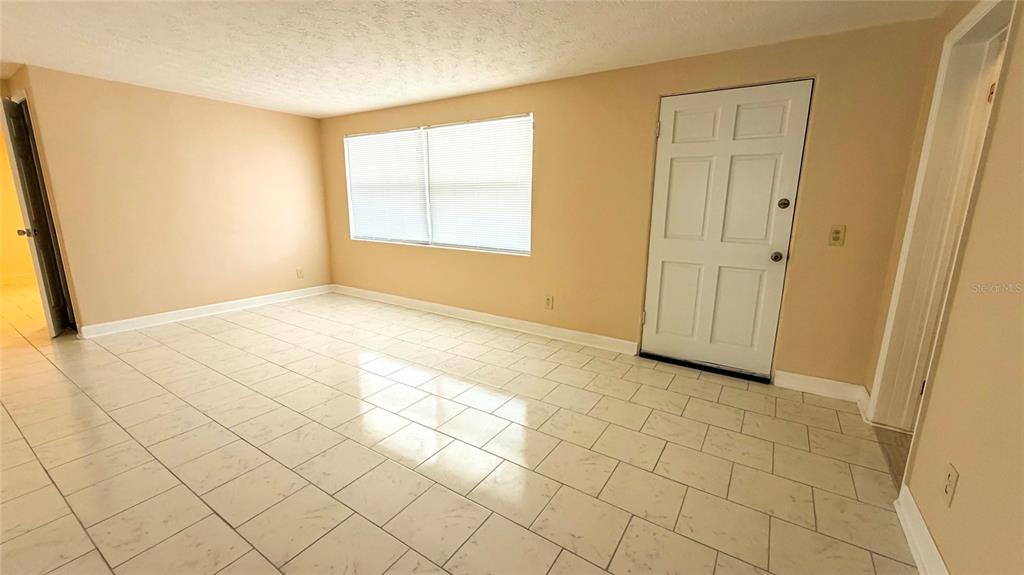 A room with light-colored tile flooring, beige walls, a window with blinds, and a door — 4102 HIGHLAND LOOP, NEW PORT RICHEY, FL