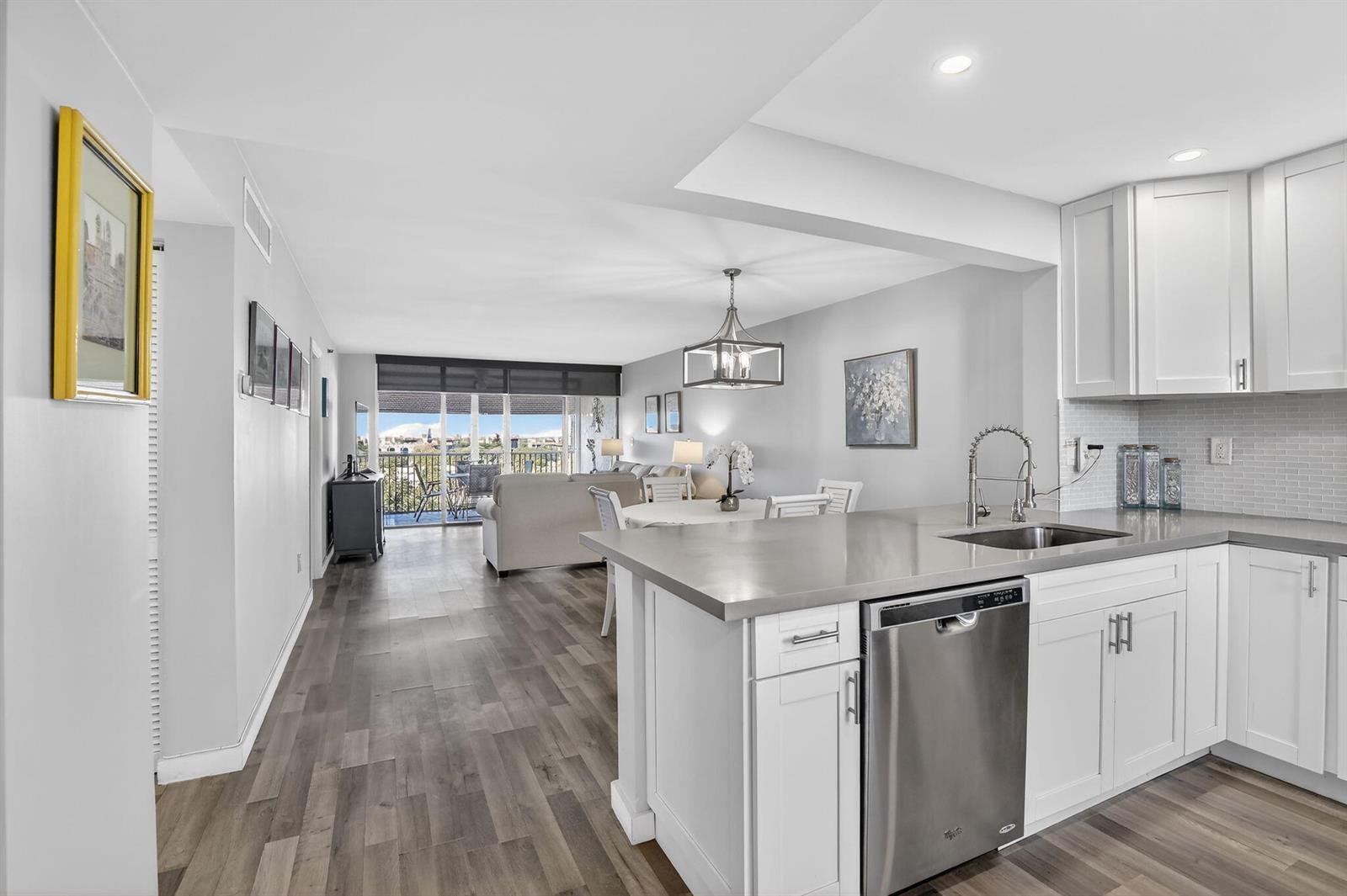 A kitchen with white cabinets and gray countertops overlooks an open living and dining area — 3910 Inverrary Boulevard # b, Lauderhill FL 33319, LAUDERHILL, FL