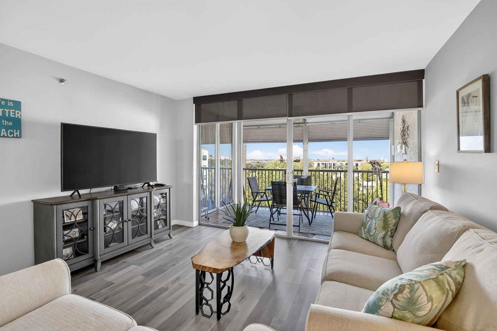 A living room features light wood flooring, a television console, and a balcony with seating — 3910 Inverrary Boulevard # b, Lauderhill FL 33319, LAUDERHILL, FL