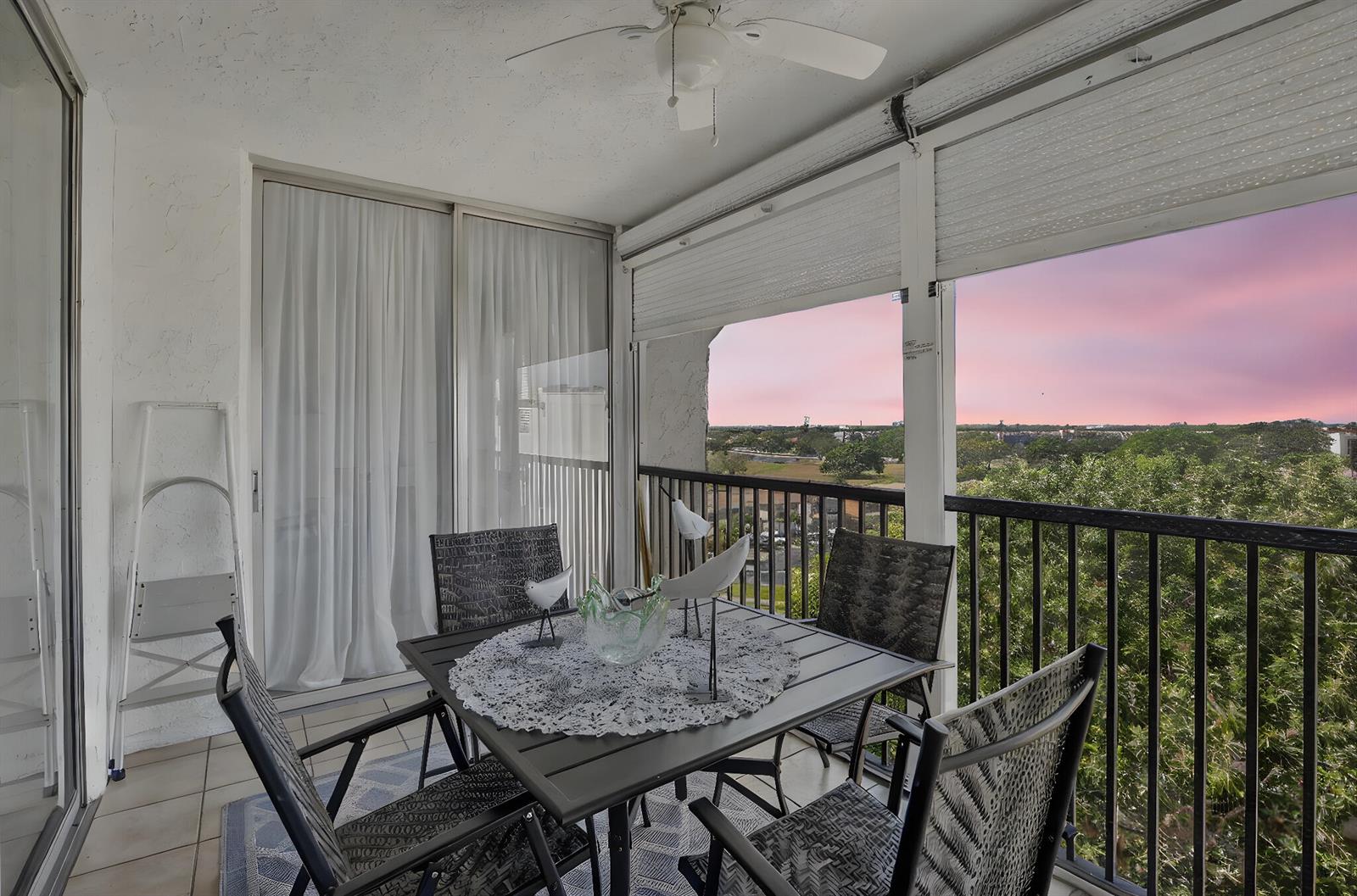 A balcony with a dining set, ceiling fan, and a view of trees at sunset — 3910 Inverrary Boulevard # b, Lauderhill FL 33319, LAUDERHILL, FL