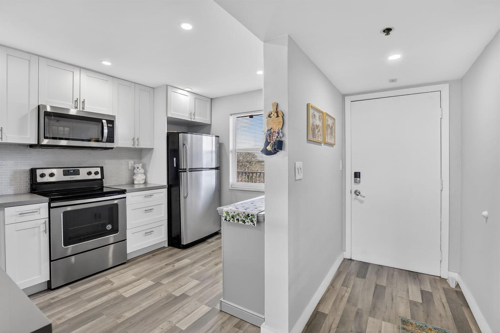 A kitchen with white cabinets, stainless steel appliances, and wood-look flooring near an entryway — 3910 Inverrary Boulevard # b, Lauderhill FL 33319, LAUDERHILL, FL