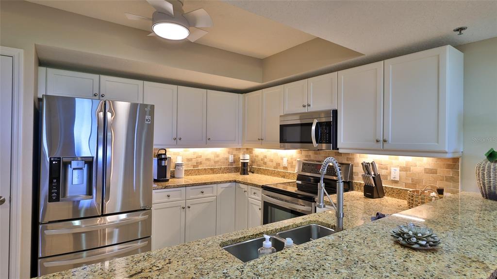 A kitchen features white cabinets, granite countertops, stainless steel appliances, and a tiled backsplash — 5300 S ATLANTIC AVENUE UNIT 16-602, NEW SMYRNA BEACH, FL