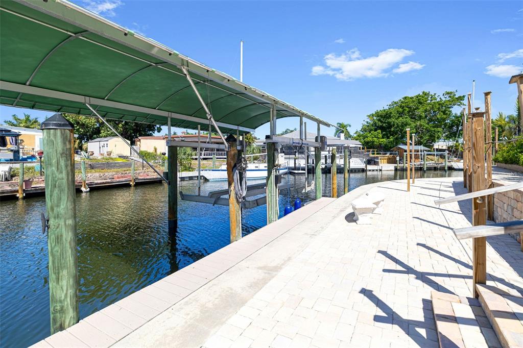A boat lift with a green canopy sits beside a paved dock on a canal — 302 BRYN MAWR ISLAND, BRADENTON, FL