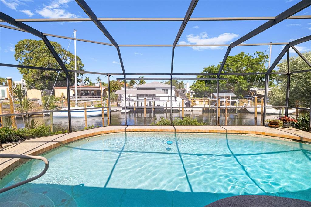 A swimming pool enclosed by a screen cage overlooks a canal with docked sailboats — 302 BRYN MAWR ISLAND, BRADENTON, FL