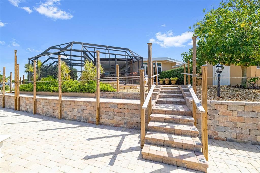 A stone retaining wall with stairs leads up to a screened-in patio area — 302 BRYN MAWR ISLAND, BRADENTON, FL