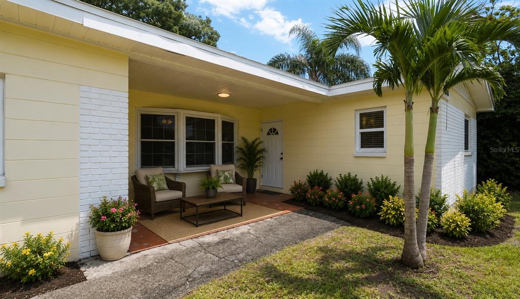 A yellow house exterior features a covered porch with seating, white brick accents, and landscaping — 2511 W VIOLET STREET, TAMPA, FL