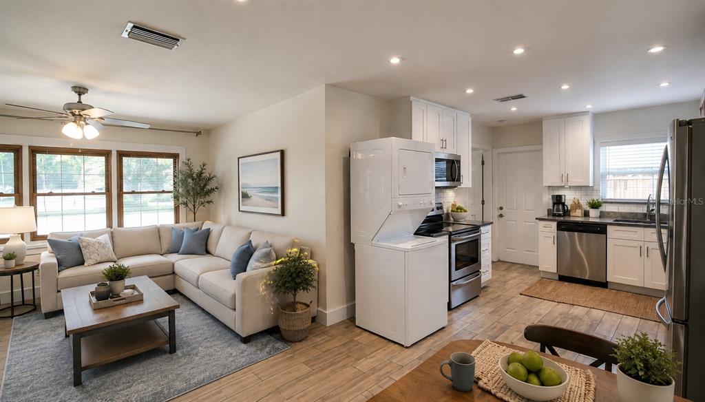 An open-concept living room and kitchen featuring light-colored cabinetry, stainless steel appliances, and wood-look flooring — 2511 W VIOLET STREET, TAMPA, FL