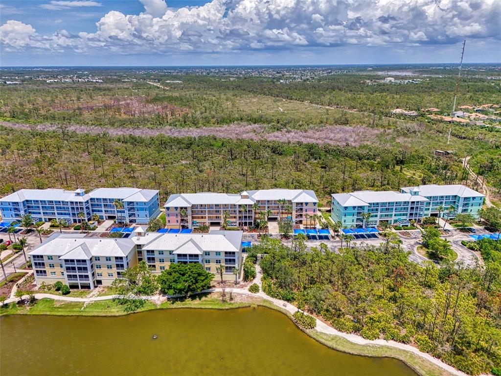 An aerial view shows several multi-story apartment buildings situated next to a pond and forest — 8409 PLACIDA ROAD UNIT 206, PLACIDA, FL