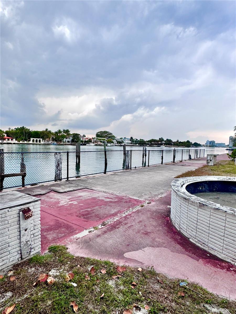 A waterfront concrete patio features a chain-link fence, a circular brick planter, and distant buildings — 5255 Collins Ave Boat Slip E, Miami Beach FL 33140, MIAMI BEACH, FL