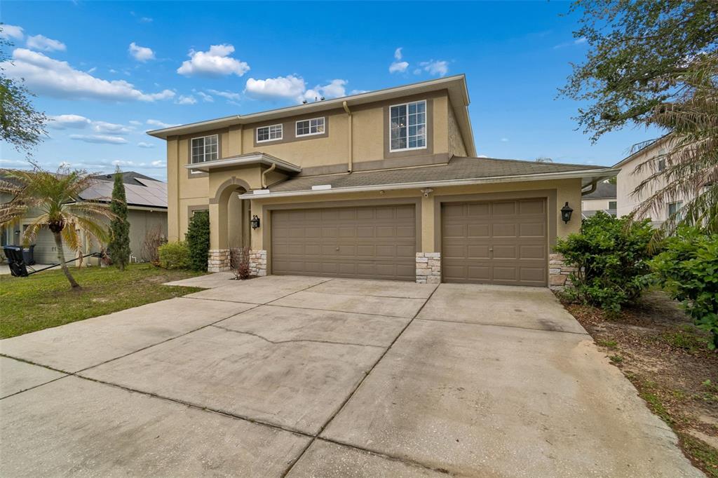 A two-story house with a tan stucco exterior, stone accents, and a three-car garage — 2829 PANKAW LANE, VALRICO, FL