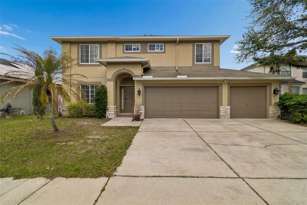 A two-story house with a tan stucco exterior, a three-car garage, and a palm tree — 2829 PANKAW LANE, VALRICO, FL