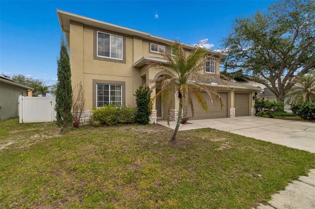A two-story house with a tan stucco exterior, a three-car garage, and a palm tree — 2829 PANKAW LANE, VALRICO, FL
