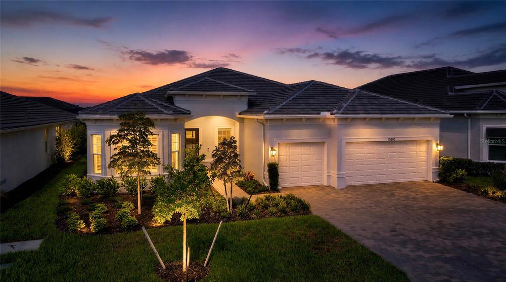 A single-story house with a paved driveway, two-car garage, and landscaped yard at sunset — 10105 BEACHWALK DRIVE, ENGLEWOOD, FL