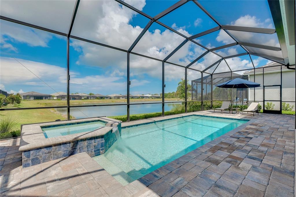 A screened-in pool and spa with brick pavers overlooking a lake under a blue sky — 10105 BEACHWALK DRIVE, ENGLEWOOD, FL