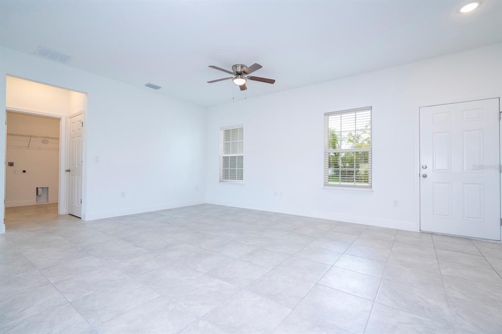 A bright, empty room with white walls, light tile flooring, a ceiling fan, and windows — 15026 SW 24TH CIRCLE, OCALA, FL