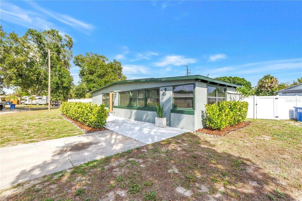 A single-story house with gray siding, green trim, and a concrete walkway in the yard — 7599 MEADOWLAWN DRIVE N, ST PETERSBURG, FL