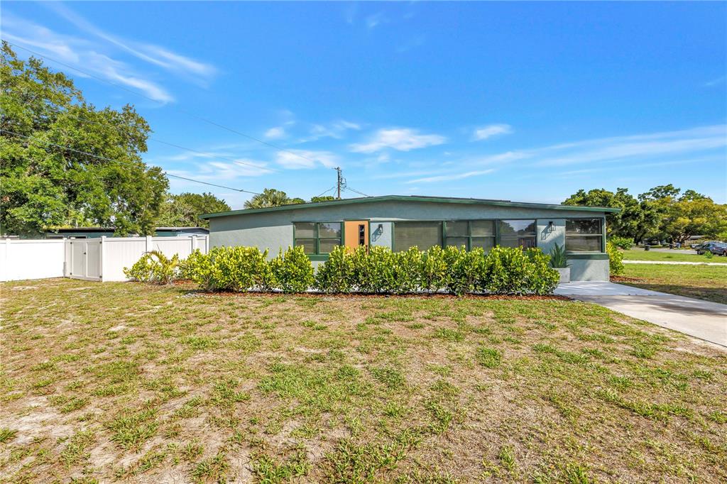 A single-story house with a green exterior, a front hedge, and a white privacy fence — 7599 MEADOWLAWN DRIVE N, ST PETERSBURG, FL