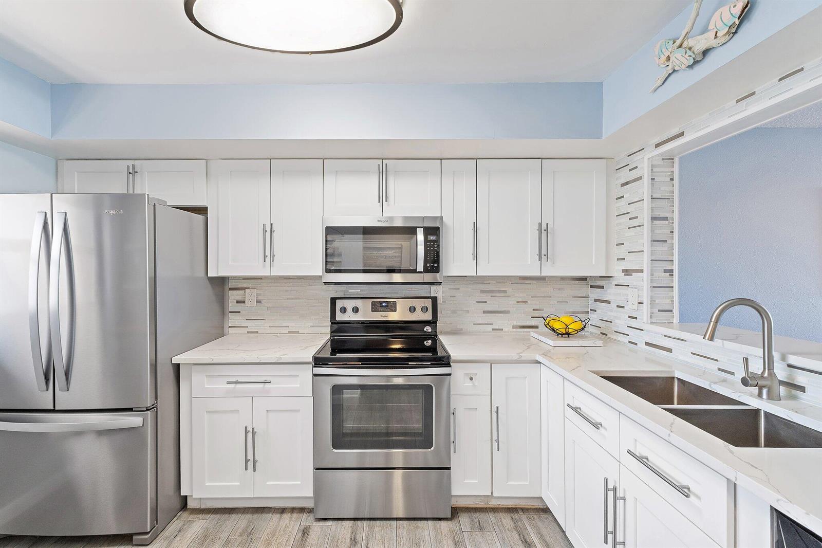 A kitchen features white cabinets, stainless steel appliances, a tiled backsplash, and light countertops — 10310 S Ocean Drive # 205, Jensen Beach FL 34957, JENSEN BEACH, FL